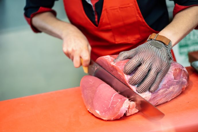 Woman cutting fresh meat in a butcher shop with metal safety mesh glove