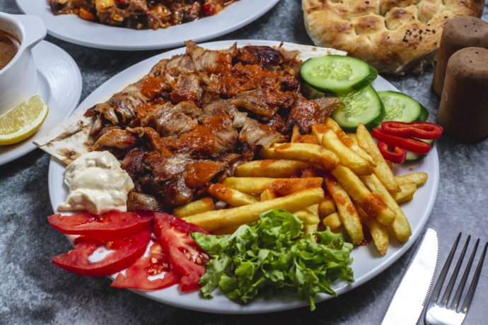 side view iskander doner on a plate with french fries tomato fresh cucumber yogurt and bread on the table